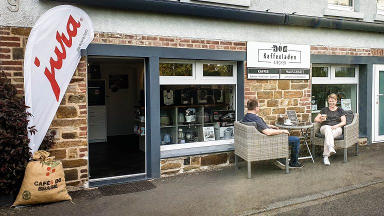 Kaffeeladen-Kirchen Aussenansicht Aussenansicht des Kaffeeladen-Kirchen mit Gästen draußen, bequemen Stühlen und einem großen Jura-Schild.